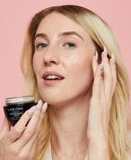 Woman holding ADVANCED GÉNIFIQUE NIGHT CREAMon on a dark pink background