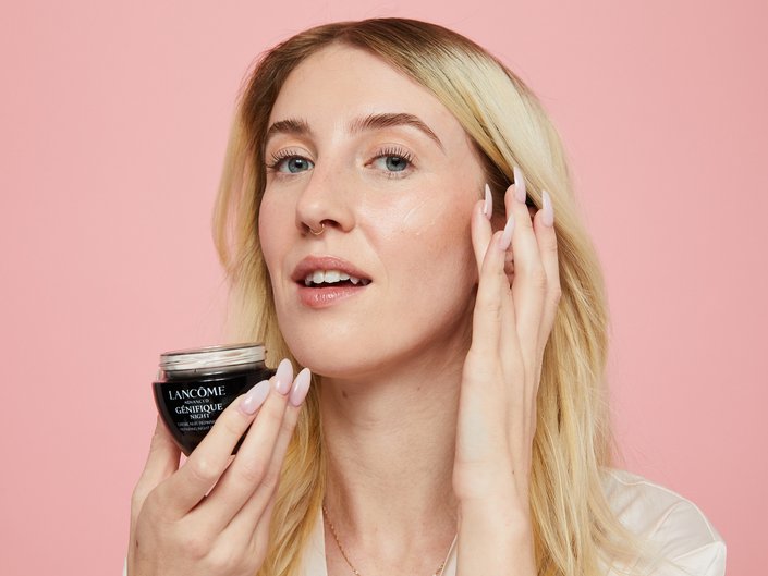 Woman holding ADVANCED GÉNIFIQUE NIGHT CREAMon on a dark pink background