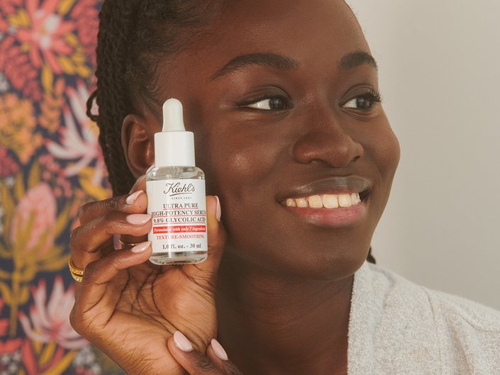 Picture of a model smiling and holding a bottle fo Kiehl's serum