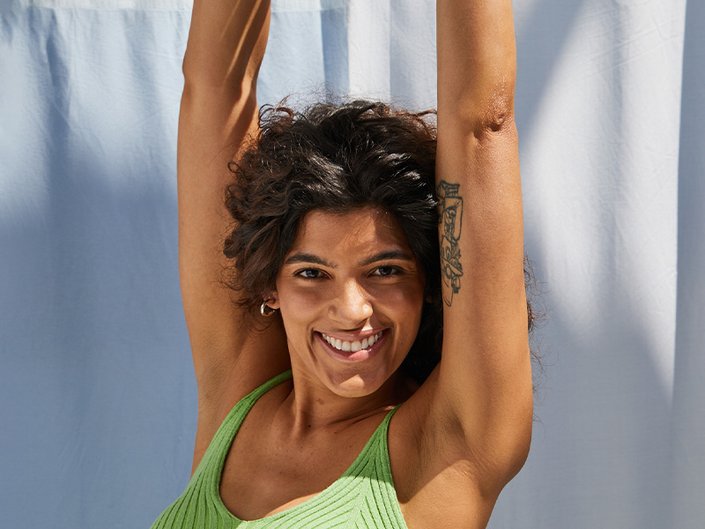 Picture of a model smiling, wearing a tank top with their arms raised above their head