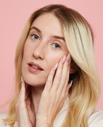 Picture of a blonde person touching the sides of their face against a pale pink background