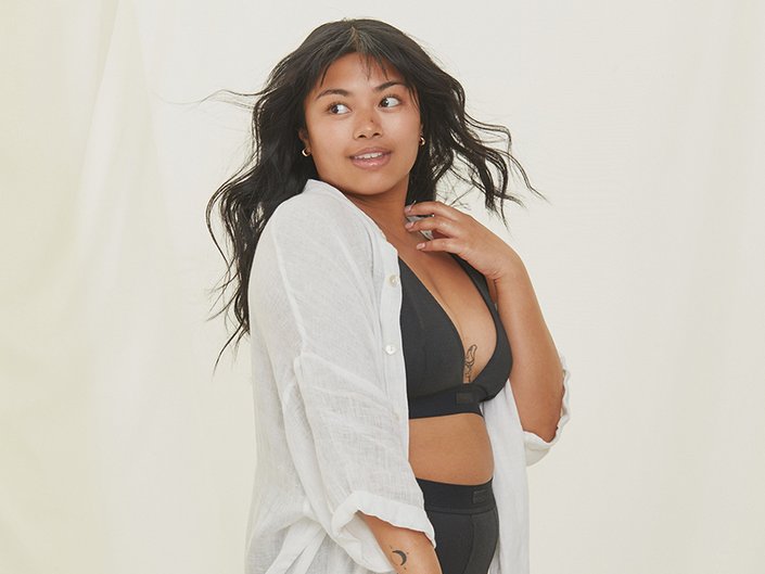 Photo of a model wearing a white button-down and black bralette, turned to the side