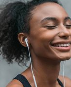 Person with dark hair pulled back in a ponytail smiling with their eyes closed and wearing earphones 